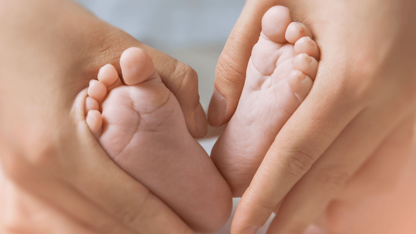 A healthcare professional gently cradling a premature infant's feet, symbolizing the vulnerable lives saved by donor milk donations through the #HumanMilk4Life campaign.