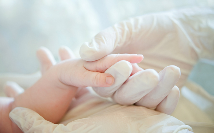 A NICU nurse's gloved hand cradling a premature infant's hand, symbolizing the dedicated care and precision behind targeted nutritional strategies.
