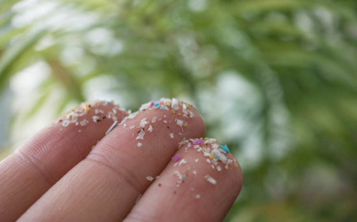 A human finger with tiny microplastic particles, illustrating how these invisible pollutants can be directly touched and ingested.